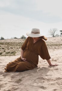 zwangere vrouw zittend in het zand